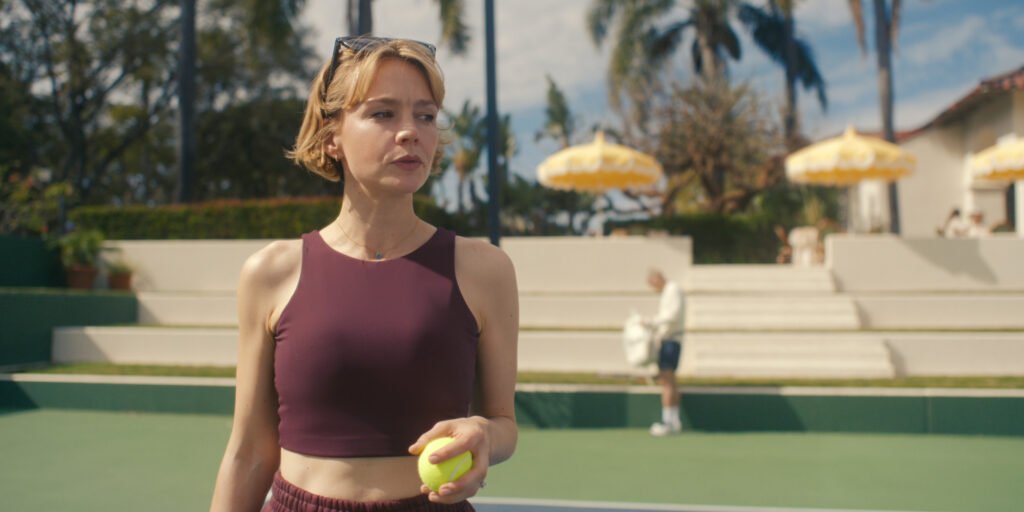 "Woman in athletic wear holding a tennis ball on an outdoor tennis court with palm trees, yellow umbrellas, and steps in the background under sunny skies."